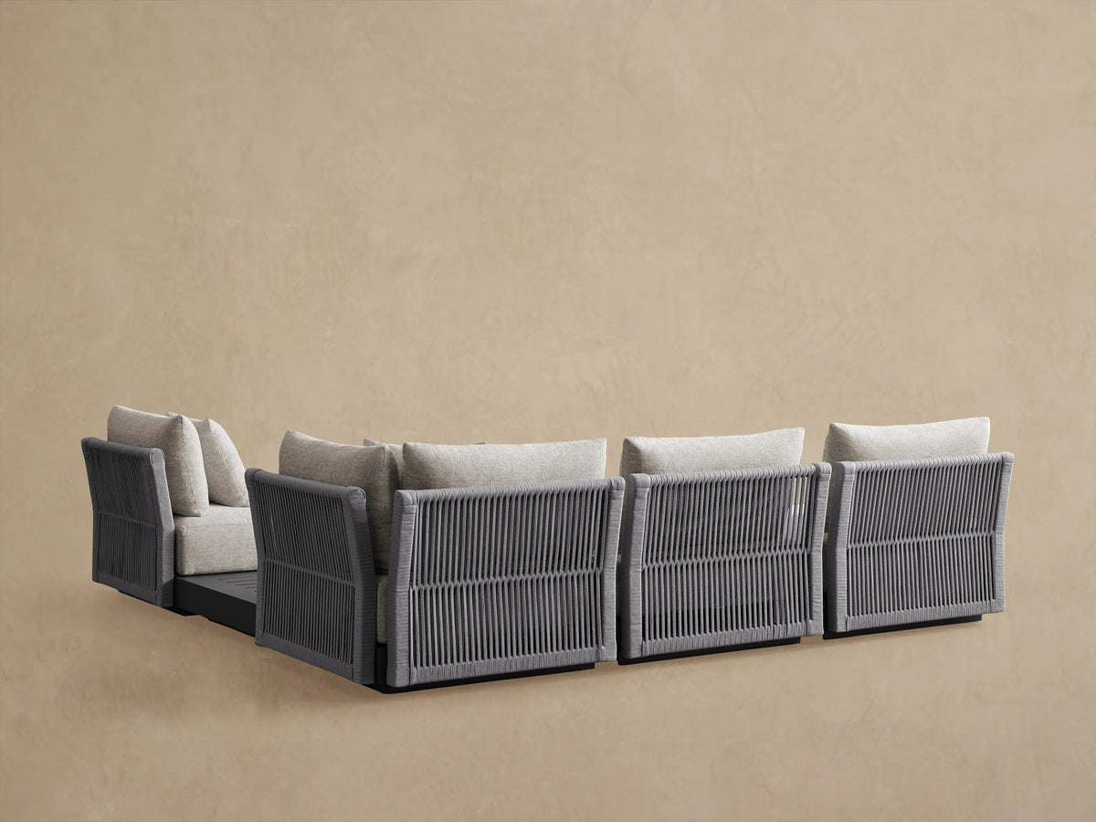 Close-up of Naxos Outdoor Five-Piece Sectional in light gray with dark gray frame and slatted side table, against a beige wall.