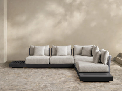 Naxos Outdoor Seven-Piece Sectional: L-shaped, dark gray aluminum frame, light gray cushions, integrated slatted side table, woven armrest, on a patio.
