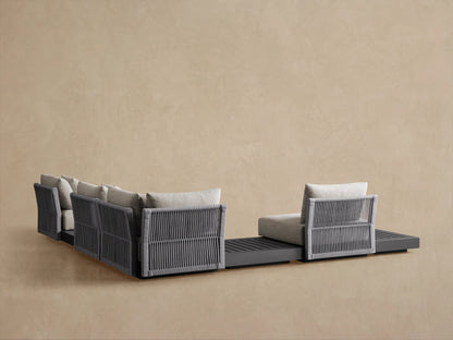 Naxos Outdoor Sectional, close-up of corner. Light grey textured cushions on dark grey aluminum frame with woven side detail.
