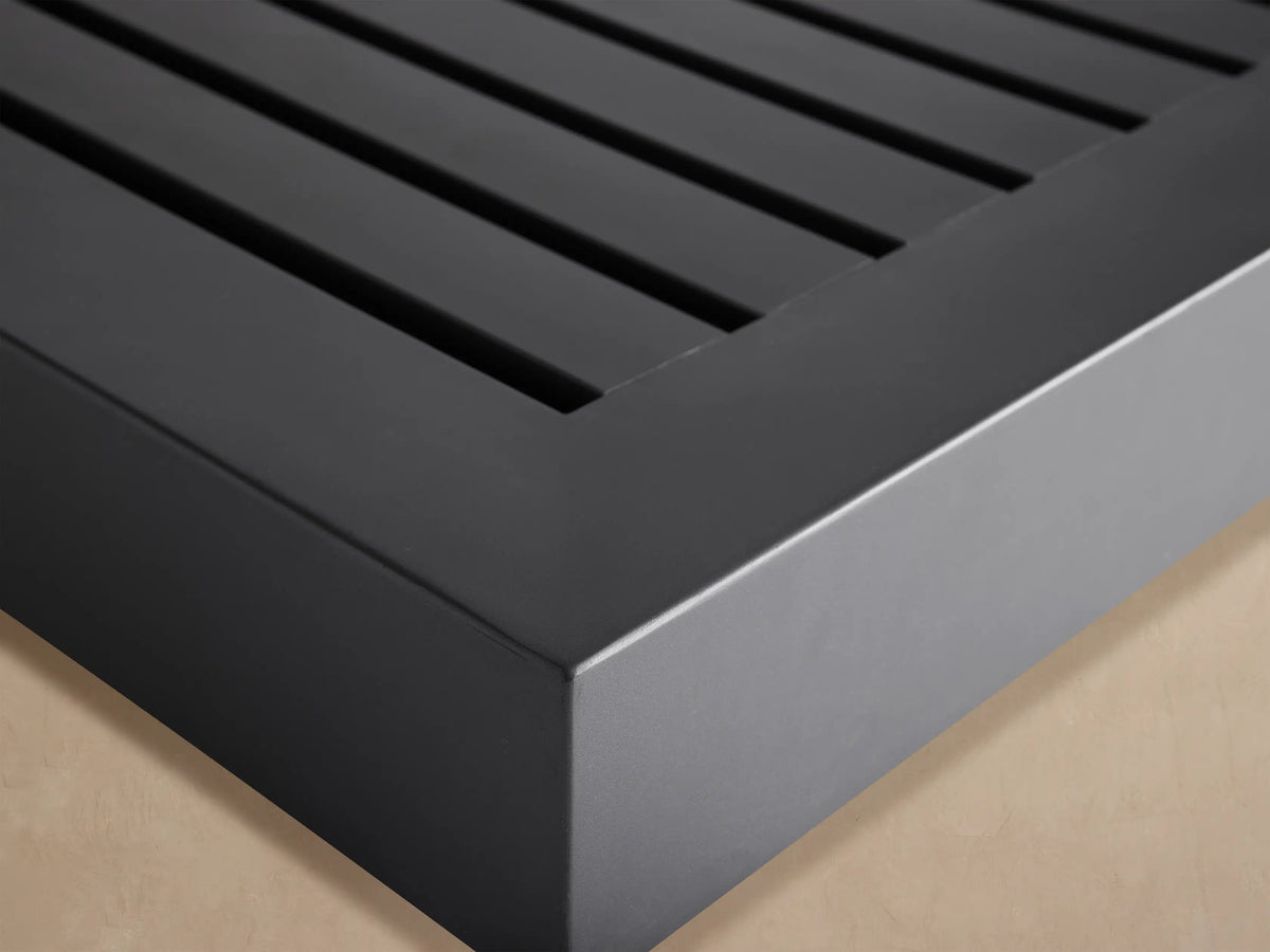 Dark grey Naxos Outdoor Double Coffee Table, low-profile, with two slatted tops, on a light stone patio in an outdoor setting.