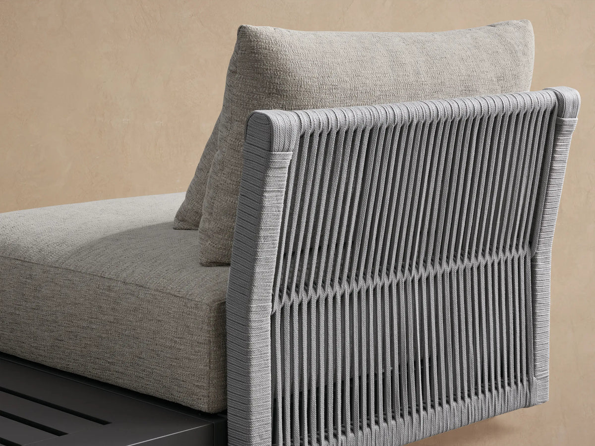Naxos Outdoor Three-Piece Sectional with dark gray frames, light gray cushions, and slatted end table on a beige patio.
