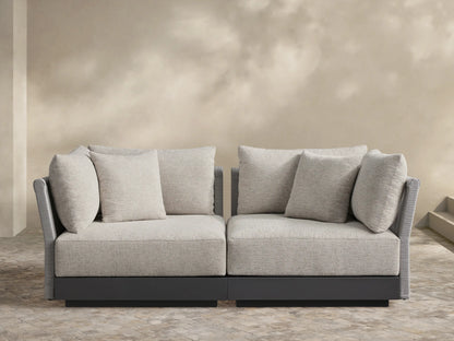 Naxos Two-Piece Modular Sofa with light gray textured cushions, dark gray frame, and ribbed arms on a stone patio.