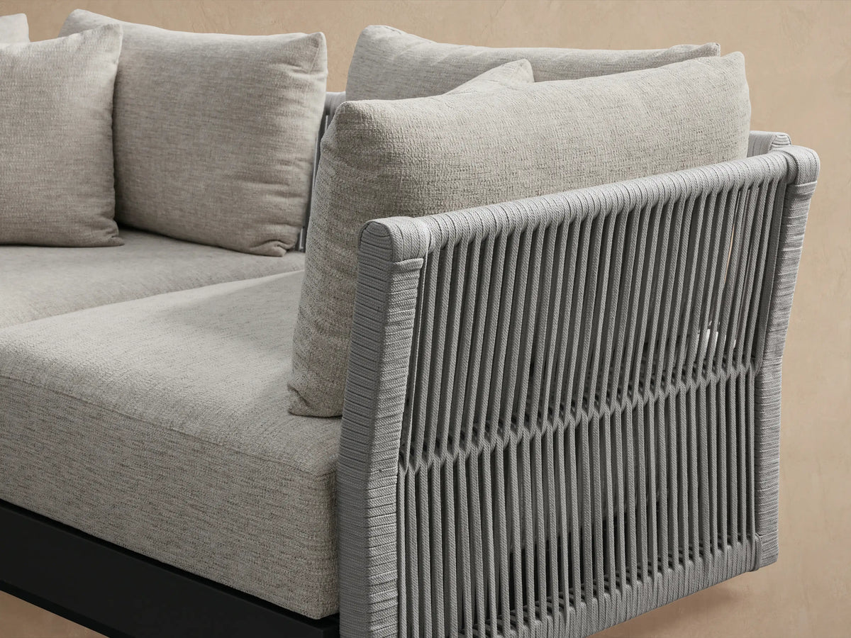 Naxos Outdoor Two-Piece Modular Sofa, light gray cushions on dark gray frame with slatted side panels, on stone patio.