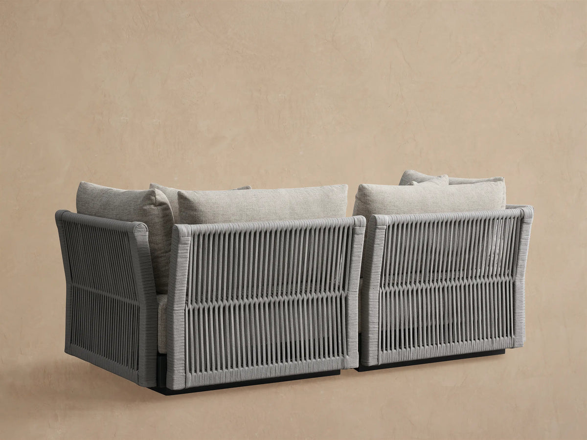 Angled close-up of Naxos Outdoor Modular Sofa. Light gray fabric cushions, dark frame, and gray rope woven side panel.