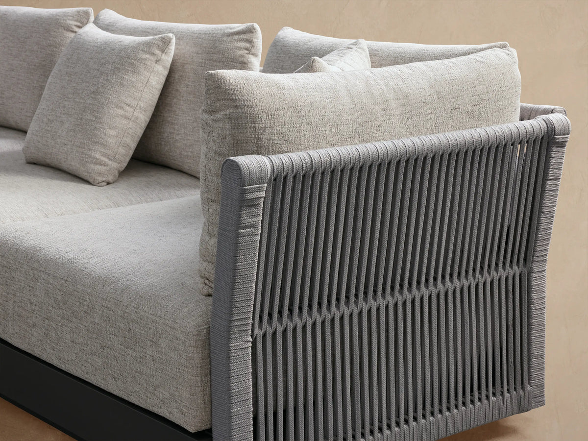 Naxos Outdoor Three Piece Modular Sofa with charcoal frame, woven armrest, and light grey fabric cushions on a tan tiled patio.