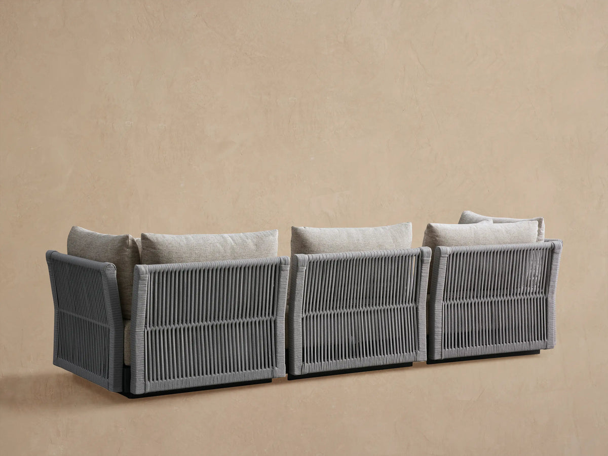 Close-up of Naxos Outdoor Modular Sofa's light grey textured cushions and dark grey woven rope side panel.