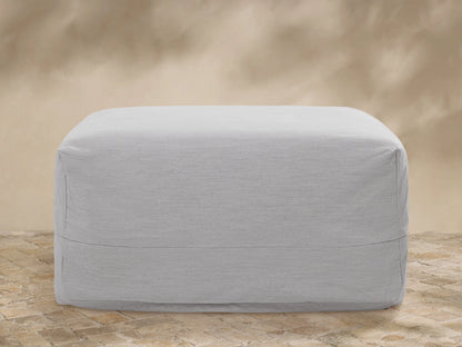 Light gray Naxos Outdoor Collection Covers on a sofa, lounge chair, and table on a stone patio with plants and a tan wall.