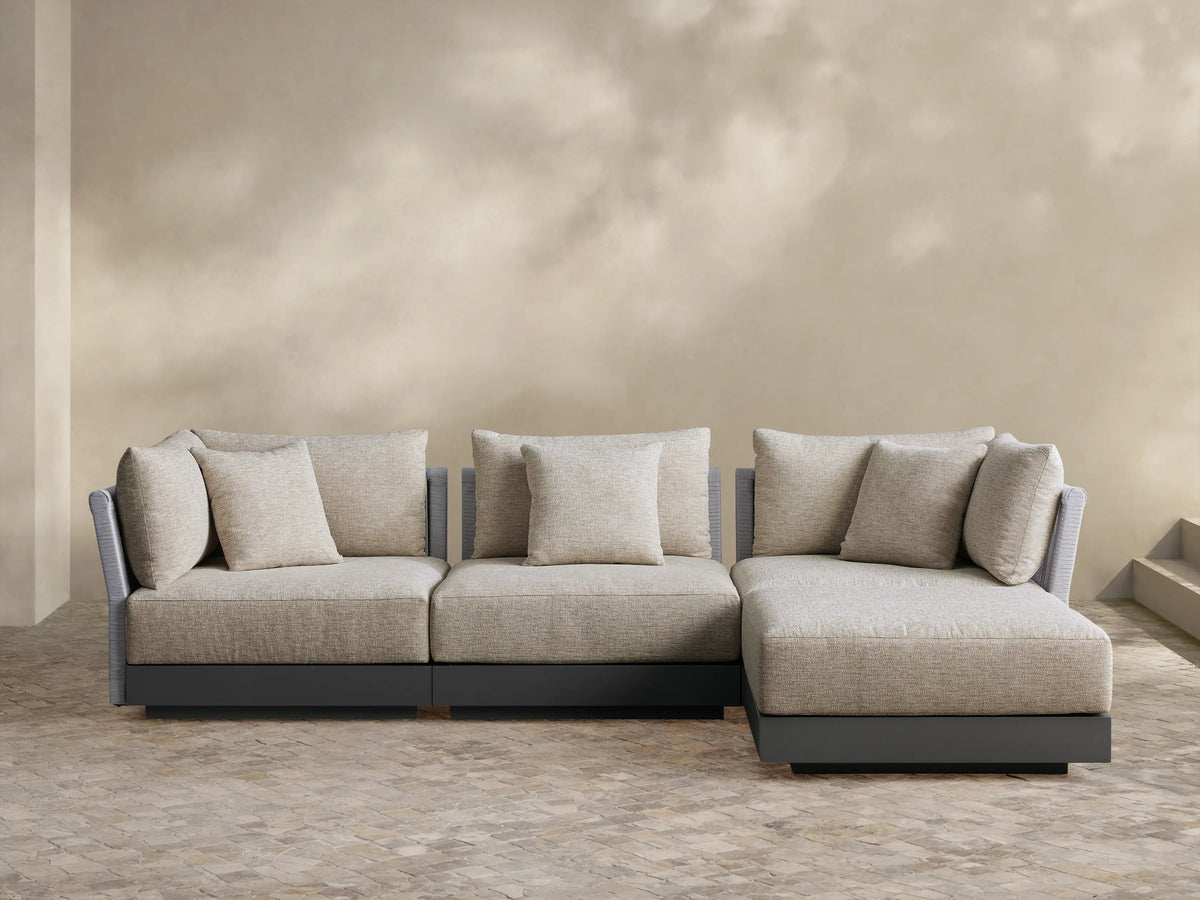Naxos outdoor four-piece sectional: light beige fabric cushions, gray textured armrests, charcoal base, L-shaped on a paver patio.
