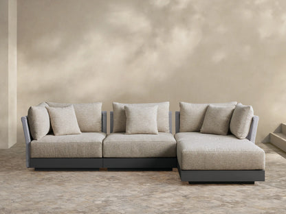 Naxos outdoor four-piece sectional: light beige fabric cushions, gray textured armrests, charcoal base, L-shaped on a paver patio.