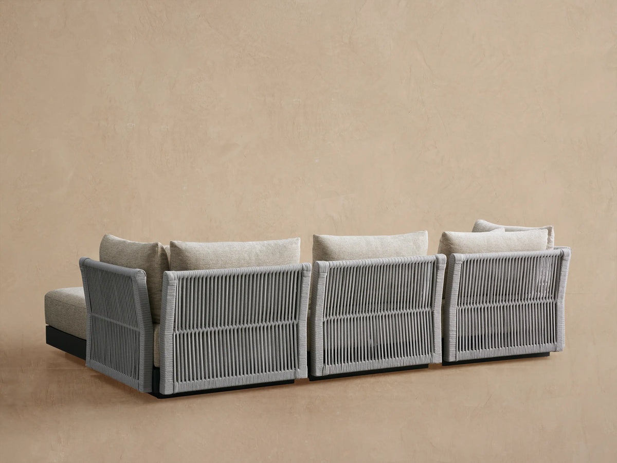 Angled view of Naxos Outdoor Sectional corner with gray woven rope armrest/back & light beige textured cushions.