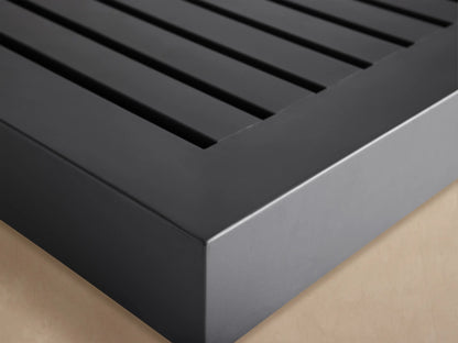Dark gray rectangular Naxos Outdoor End Table, low profile with a slatted top, on a stone patio against a light wall.