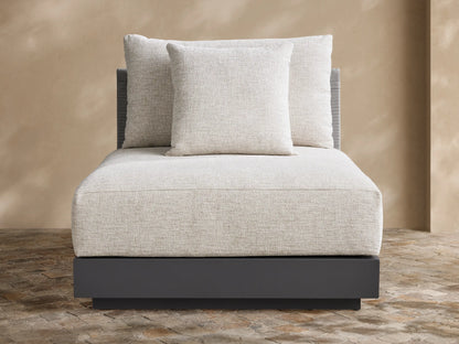 Naxos Outdoor Armless Chair with light grey textured cushions, dark charcoal base, and woven back, on a stone patio.