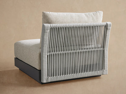 Close-up of Naxos Outdoor Armless Chair. Grey intricately woven rope backrest, light beige textured fabric seat and back cushions against a warm wall.