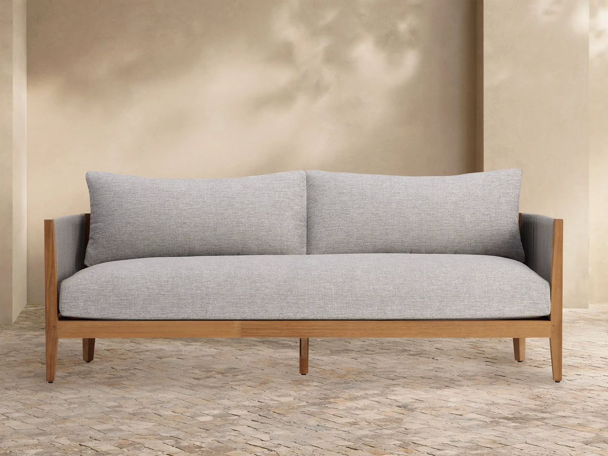 Light gray Newport Outdoor Collection Cover tailored over a long outdoor furniture piece, on a stone patio against a beige wall.