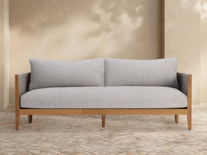 Light gray Newport Outdoor Collection Cover tailored over a long outdoor furniture piece, on a stone patio against a beige wall.