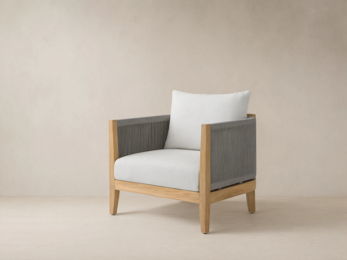 Newport Outdoor Lounge Chair with natural teak frame, dark grey woven rope arms, and light Eden Snow cushions on an outdoor patio.
