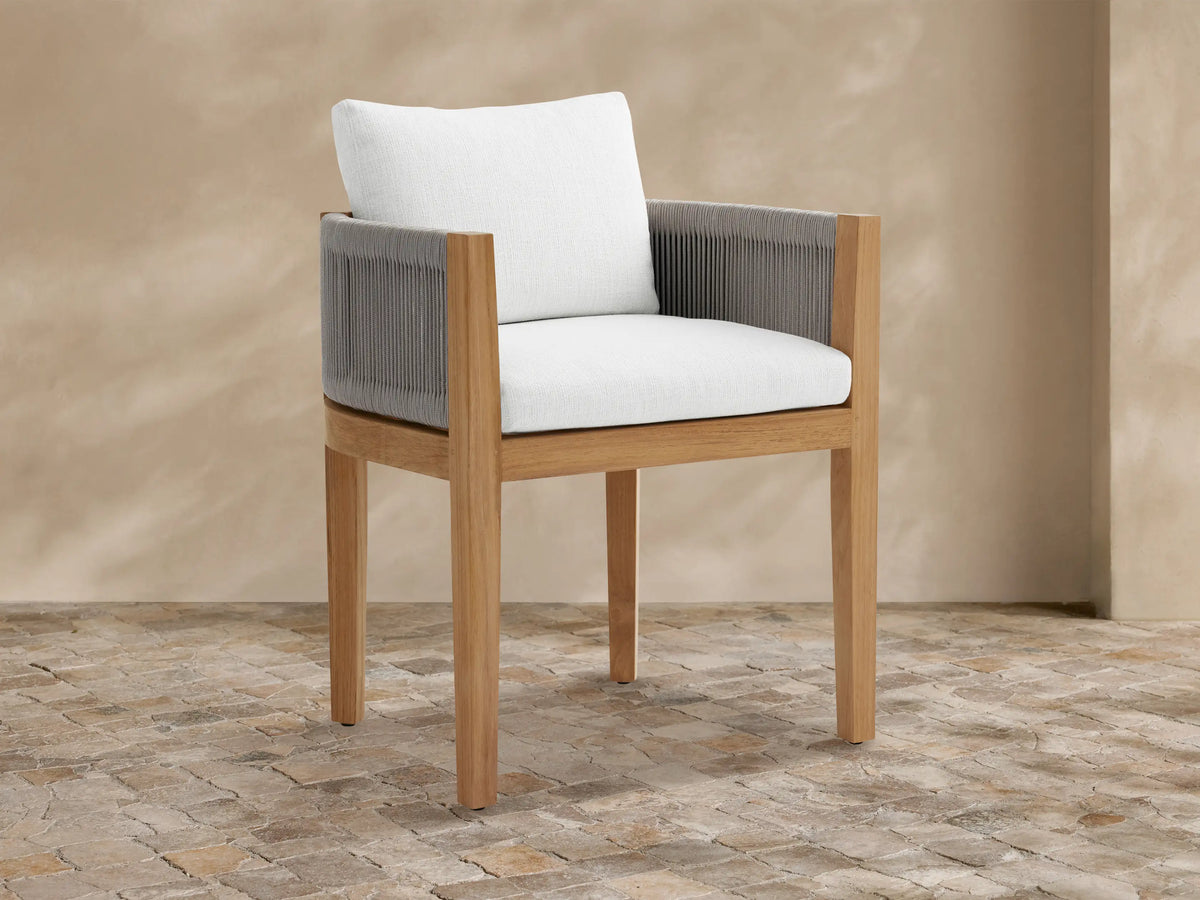 Newport outdoor dining arm chair: natural teak wood frame, gray woven rope arms, white Eden Snow cushions, on stone tile.