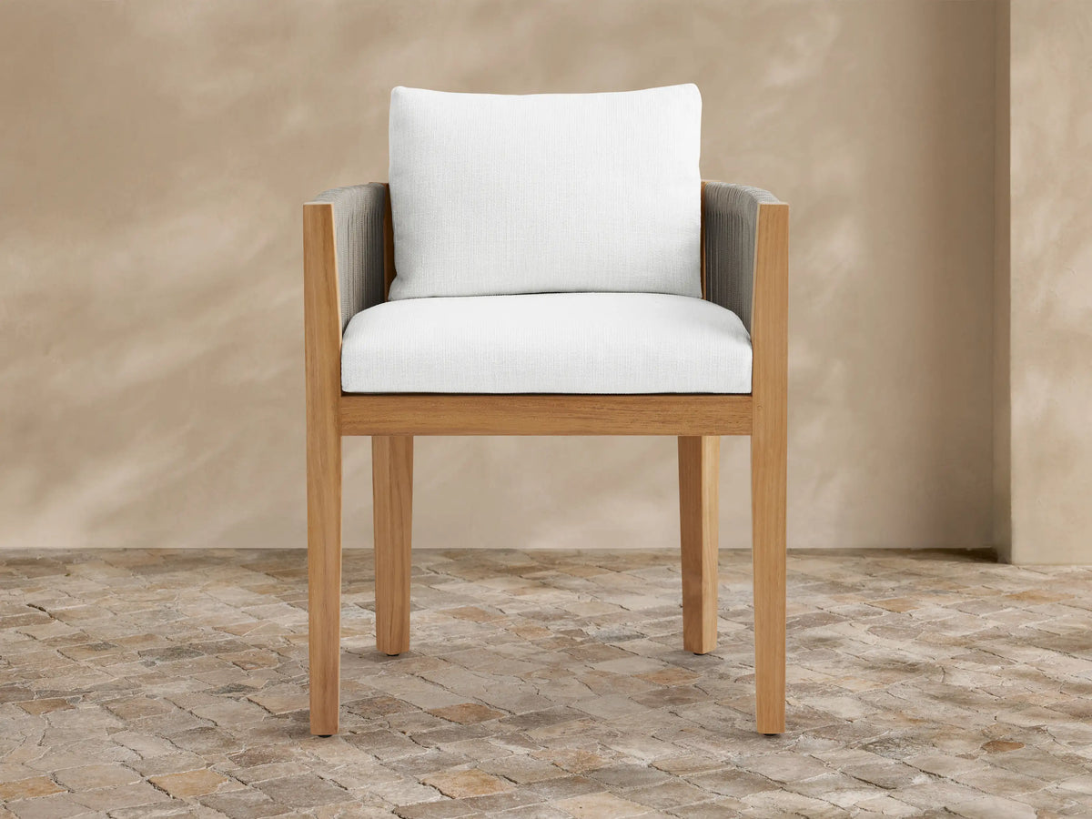 Newport outdoor dining arm chair: natural teak wood frame, gray woven rope arms, white Eden Snow cushions, on stone tile.