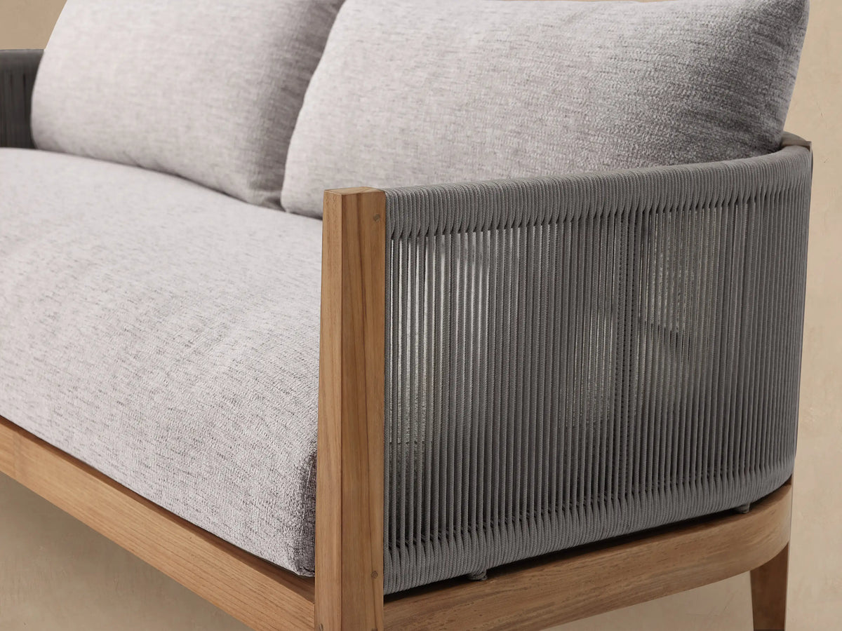 Newport Outdoor Sofa. Two-seater with natural teak frame, gray woven rope armrests, and light grey cushions in an outdoor scene.