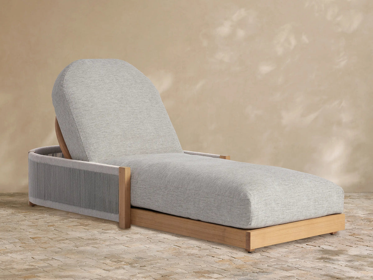 Light grey cushioned Newport Outdoor Chaise, teak frame with grey woven sides, angled on a tiled floor against a beige wall.