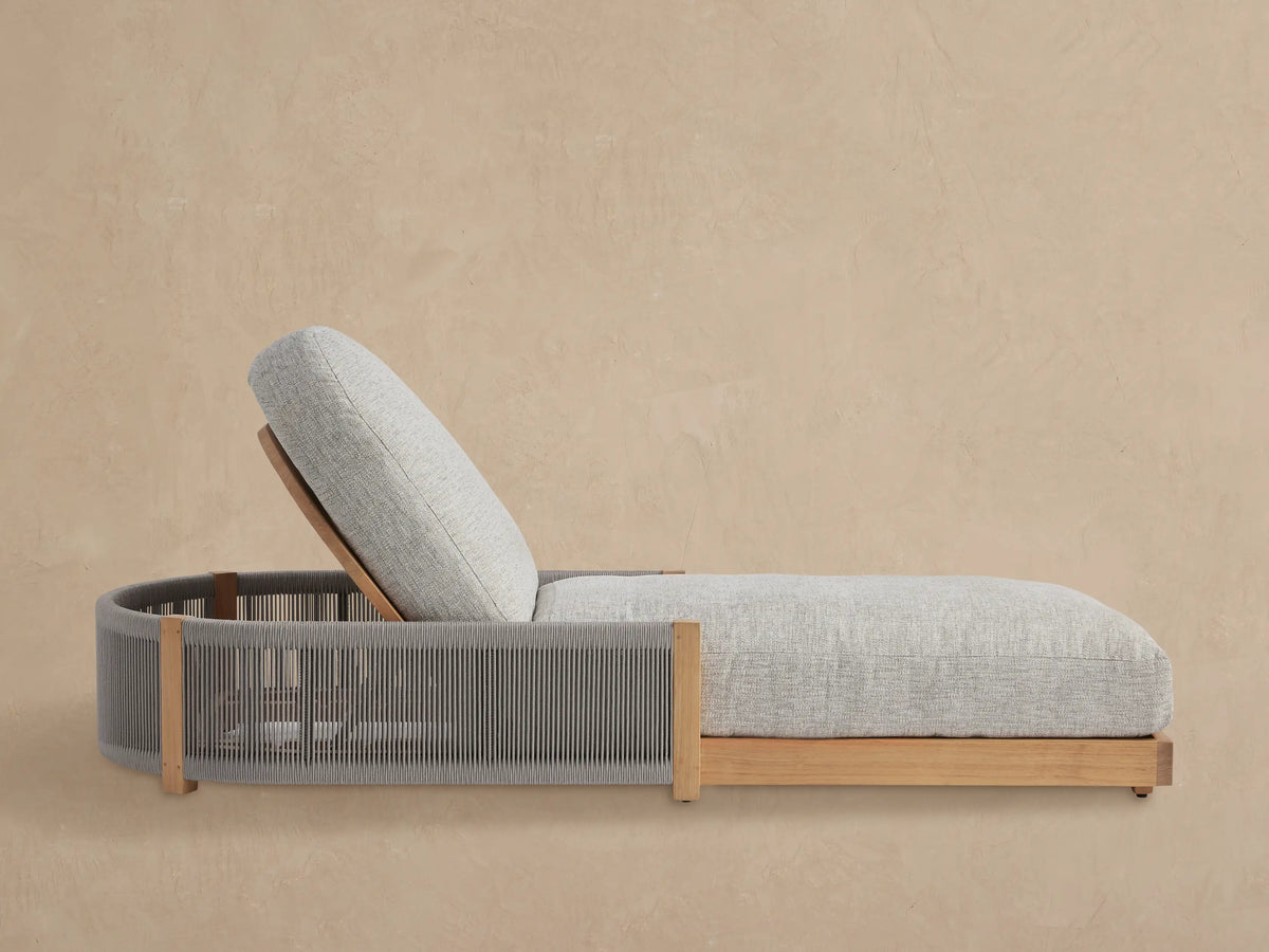 Light grey cushioned Newport Outdoor Chaise, teak frame with grey woven sides, angled on a tiled floor against a beige wall.