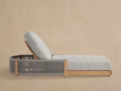 Light grey cushioned Newport Outdoor Chaise, teak frame with grey woven sides, angled on a tiled floor against a beige wall.