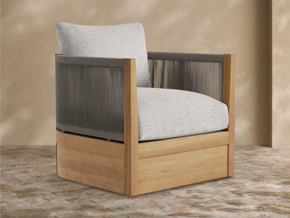 Newport Outdoor Lounge Chair with golden teak wood frame, woven gray rope arms/back, and plush light gray cushions, angled on a patio.