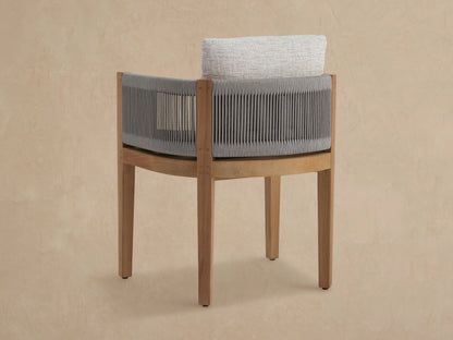 Angled close-up of Newport Outdoor Dining Arm Chair with gray rope weaving, golden-brown teak frame, and light gray cushions.