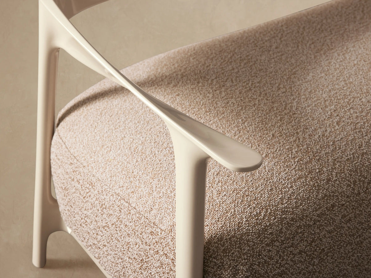Nia Outdoor Sofa: Light beige, glossy curved frame with a textured tan rectangular cushion, set on a stone tiled floor.