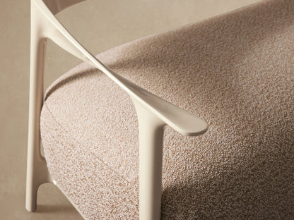 Nia Outdoor Sofa: Light beige, glossy curved frame with a textured tan rectangular cushion, set on a stone tiled floor.