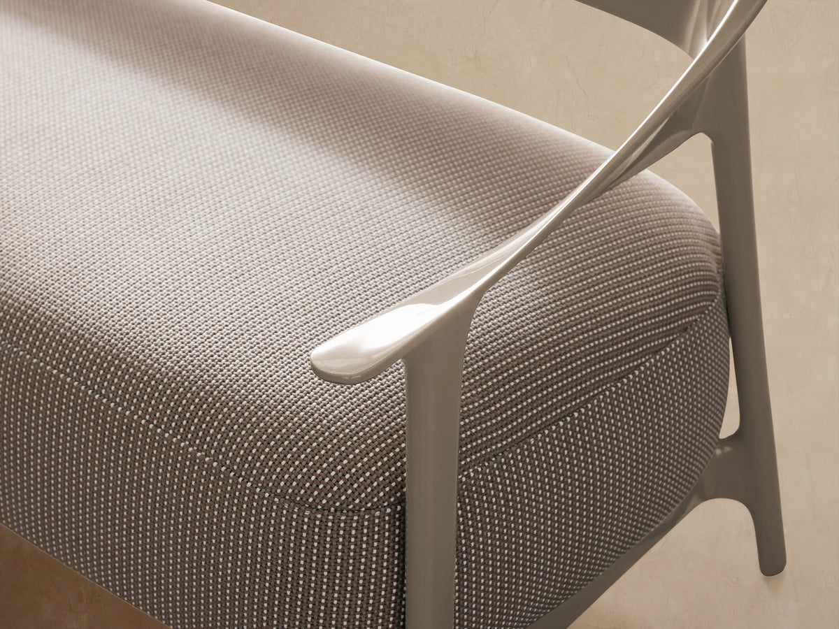 Nia Outdoor Sofa with light beige, curved frame and dark gray textured cushion, angled on a light stone floor.