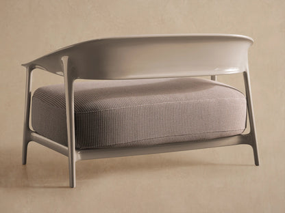Nia Outdoor Sofa close-up: textured light grey speckled cushion with a smooth, curved taupe armrest and frame.