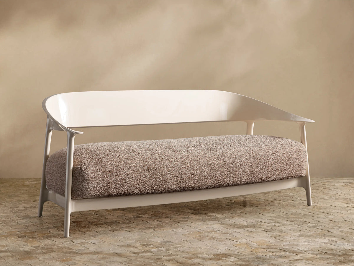 Nia Outdoor Sofa. Cream frame, curved backrest, light brown speckled cushion, against a beige wall & tiled floor.