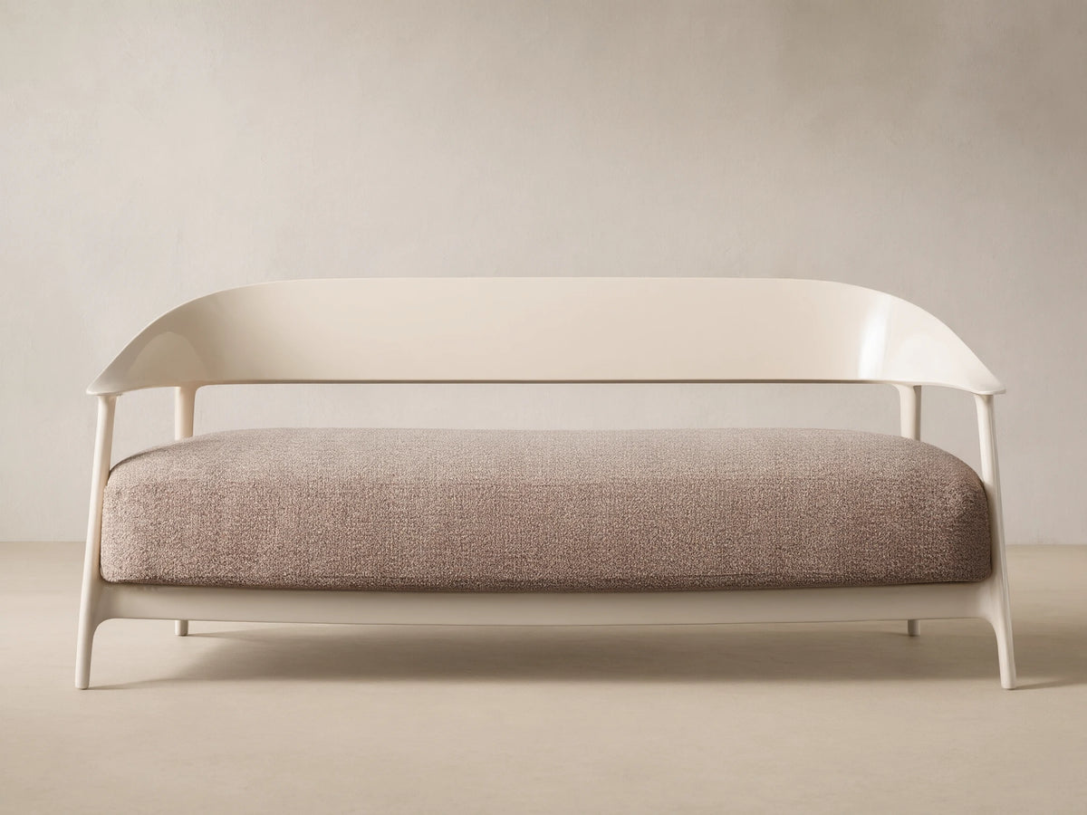 Nia Outdoor Sofa. Cream frame, curved backrest, light brown speckled cushion, against a beige wall & tiled floor.