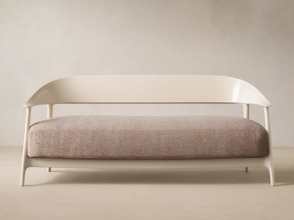 Nia Outdoor Sofa. Cream frame, curved backrest, light brown speckled cushion, against a beige wall & tiled floor.