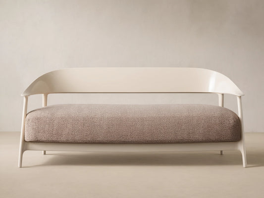 Nia Outdoor Sofa. Cream frame, curved backrest, light brown speckled cushion, against a beige wall & tiled floor.