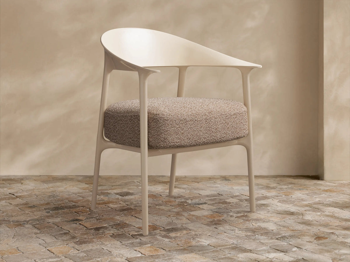 Nia Outdoor Dining Chair, light beige molded frame and speckled brown cushion, angled right on a stone tiled floor.