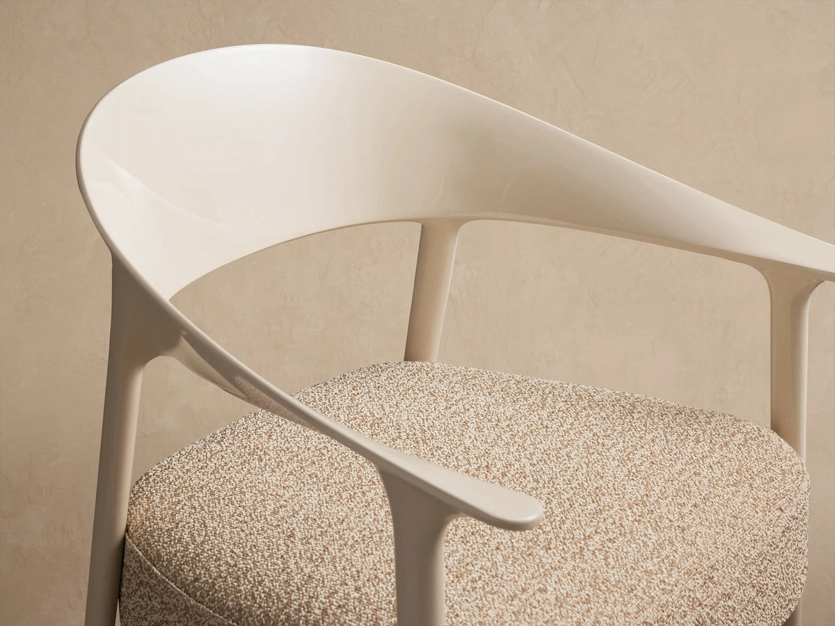 Nia Outdoor Dining Chair: Cream-colored frame, curved backrest, and speckled beige cushion on a rustic tiled floor.