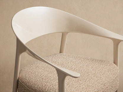 Nia Outdoor Dining Chair: Cream-colored frame, curved backrest, and speckled beige cushion on a rustic tiled floor.
