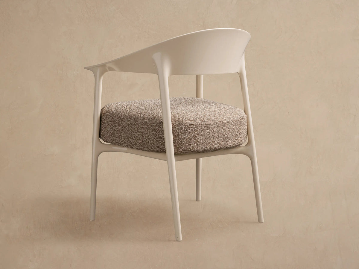 Close-up of Nia Outdoor Dining Chair: light beige frame with curved back/armrests, textured beige seat cushion, angled view.