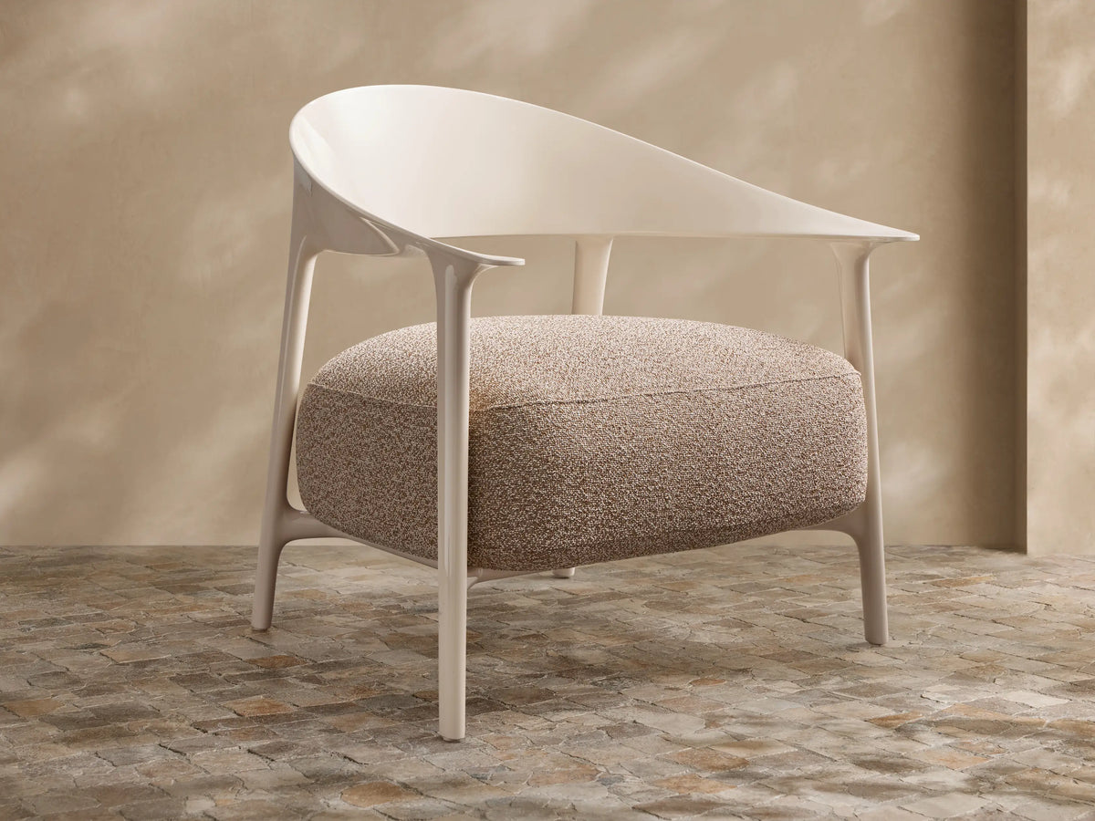 Modern Nia Outdoor Lounge Chair with an off-white molded frame and a thick, textured light brown cushion, on a stone floor.