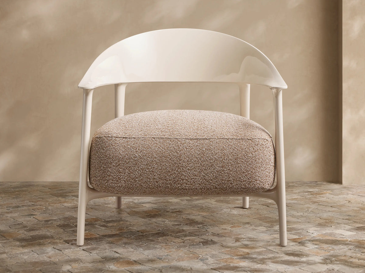 Modern Nia Outdoor Lounge Chair with an off-white molded frame and a thick, textured light brown cushion, on a stone floor.