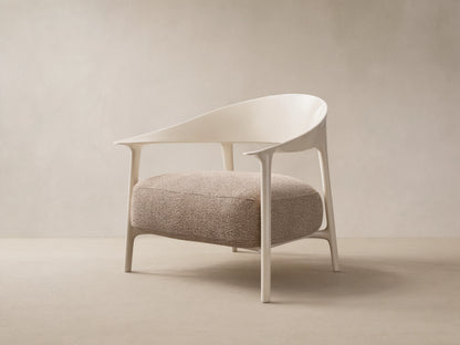 Modern Nia Outdoor Lounge Chair with an off-white molded frame and a thick, textured light brown cushion, on a stone floor.