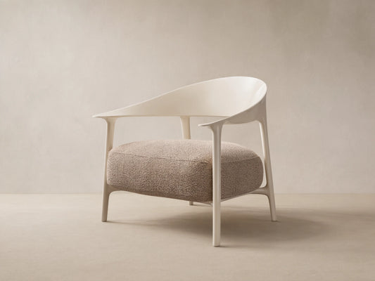 Modern Nia Outdoor Lounge Chair with an off-white molded frame and a thick, textured light brown cushion, on a stone floor.