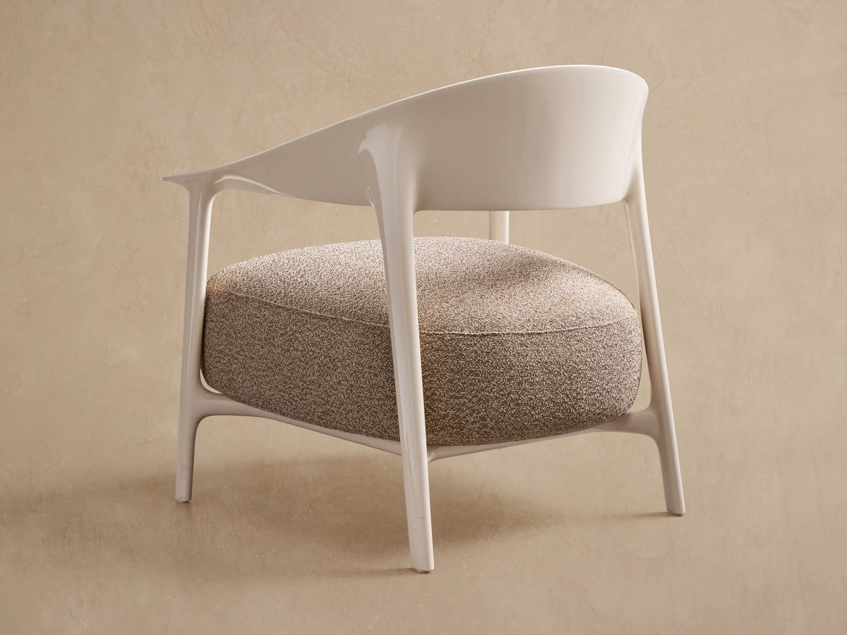 Creamy frame of Nia Outdoor Lounge Chair curves around a textured tan and brown cushion, shown in close-up.