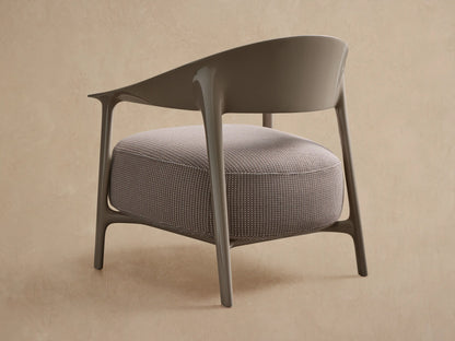 Nia Outdoor Lounge Chair. Angled view of a light taupe, glossy frame with a curved backrest & round, textured light beige cushion.