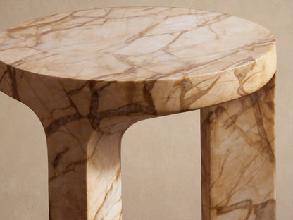 Odessa Outdoor End Table. Round end table with three thick legs, in light brown marble-look finish with veining, on a tiled patio.