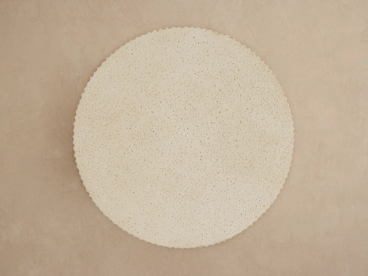 Ojai Outdoor End Table: Close-up of a round, light beige table with a textured, speckled top and deeply ribbed sides.