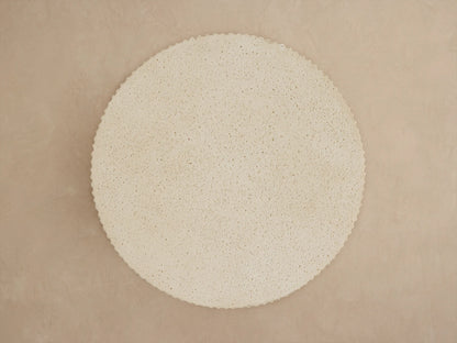 Ojai Outdoor End Table: Close-up of a round, light beige table with a textured, speckled top and deeply ribbed sides.