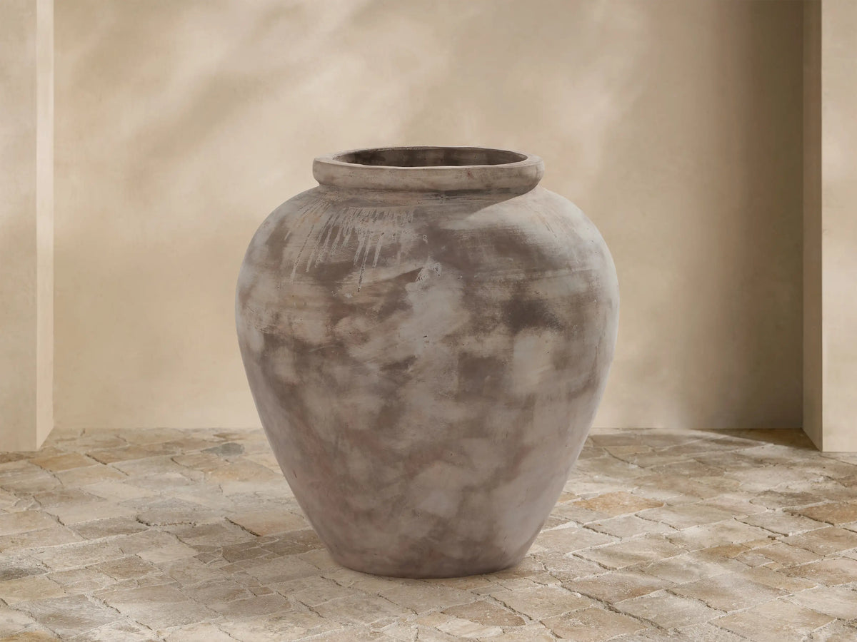 Large Olivio Outdoor Planter with weathered antico terracotta finish, rounded ceramic on light stone pavers against a beige wall.